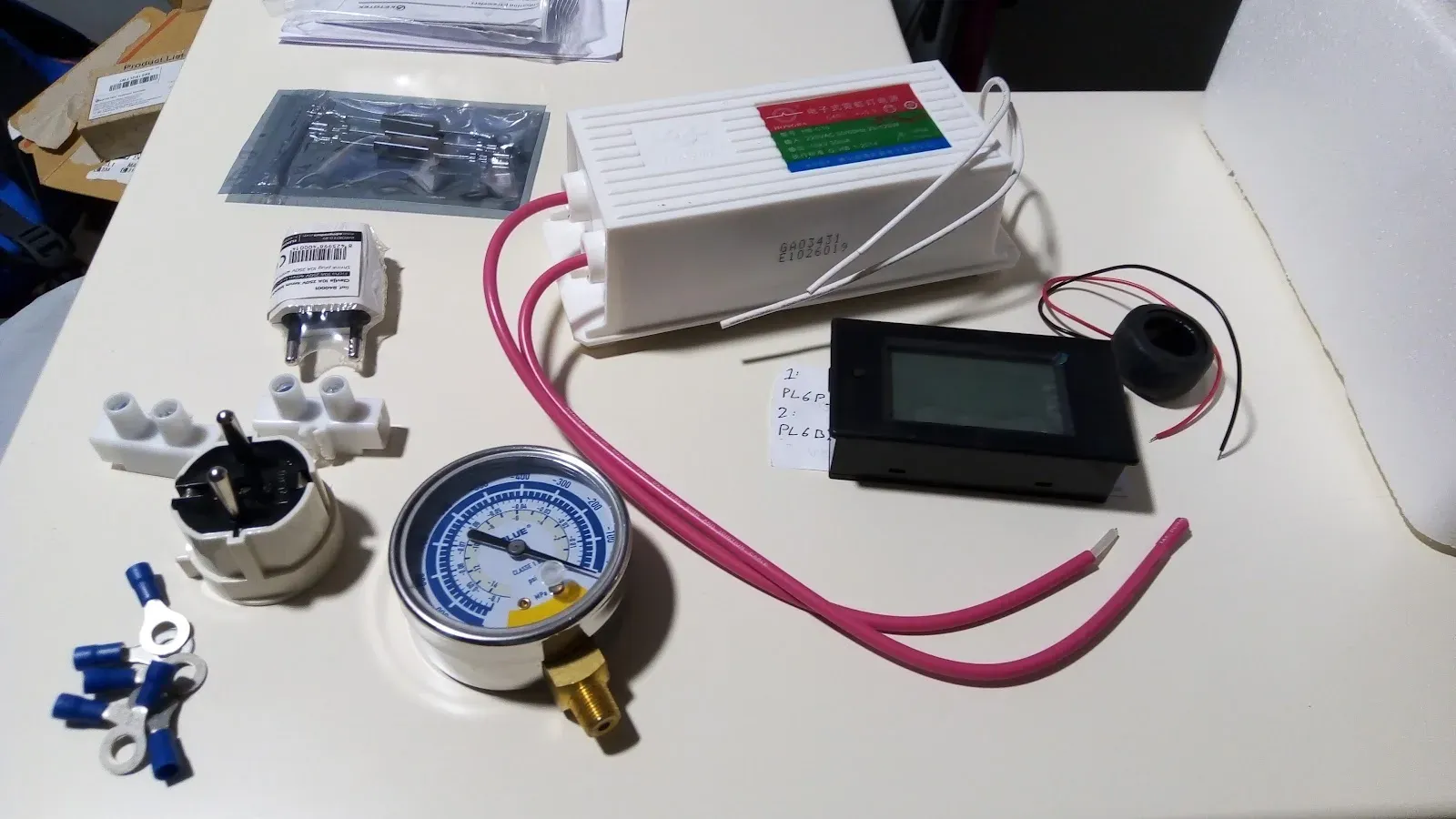 Componentes sobre la mesa: transformador de neón, manómetro, voltímetro LCD y cables